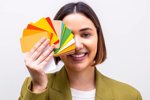 A smiling woman holds a vibrant palette of color swatches, signifying a professional image