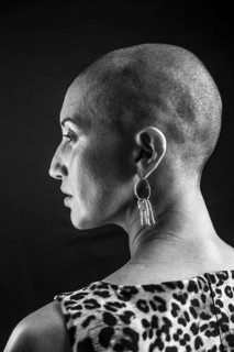 Black and white portrait of a bald woman in profile, showcasing elegant earrings and a patterned