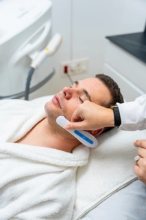 Man receiving modern facial treatment with a handheld device at an aesthetic clinic, focused on