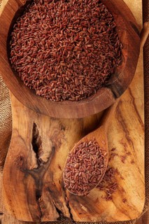 Natural, red rice, in a wooden bowl and spoon on a wooden surface in rustic style, top view