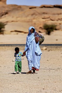 Mother and child, both in traditional dress, walking through a barren desert landscape, woman in