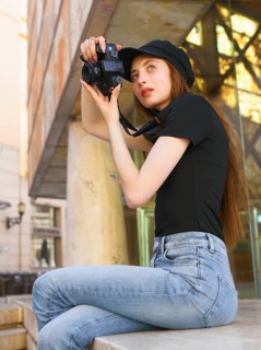A woman in casual attire takes photos with a professional camera in a city setting. Her focused