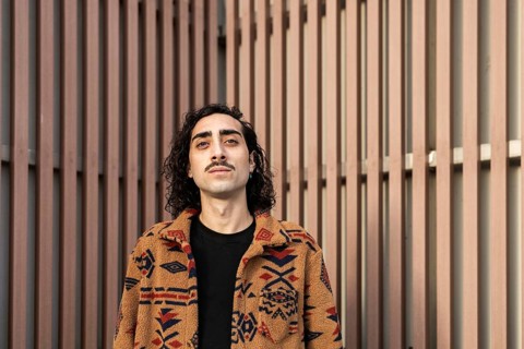 Portrait of a confident man with a mustache, wearing a patterned jacket, standing against a modern