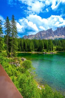 Emerald waters of lake carezza reflecting latemar mountain range in dolomites on a beautiful sunny