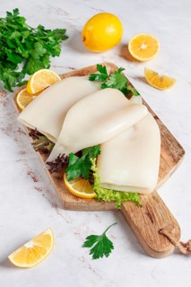 Fresh squid prepared for cooking, surrounded by herbs and lemon, placed on a wooden chopping board