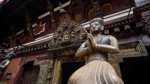 Statue of a praying figure in traditional dress against an ornate temple background, Kathmandu,