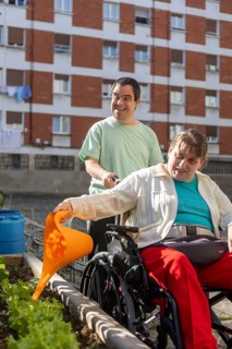 Two individuals at a day center participate in gardening, nurturing plants in an outdoor garden.