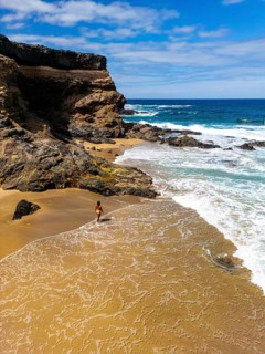From above drone view of a lone woman walks on the sandy shore of Tindaya Beach in Fuerteventura,