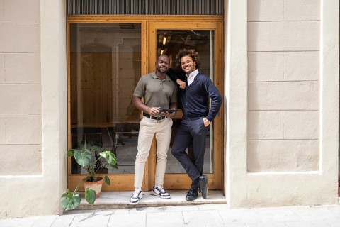 Two professionals smiling in front of a coworking space in Barcelona, showcasing a modern and