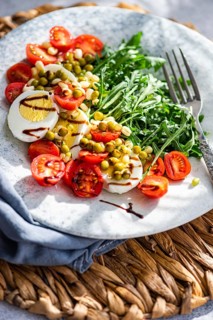 A vibrant keto lunch featuring boiled eggs, fresh rocket leaves, cherry tomatoes, canned green