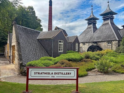 Historic Strathisla distillery with distinctive roofs and well-kept garden in rural surroundings,