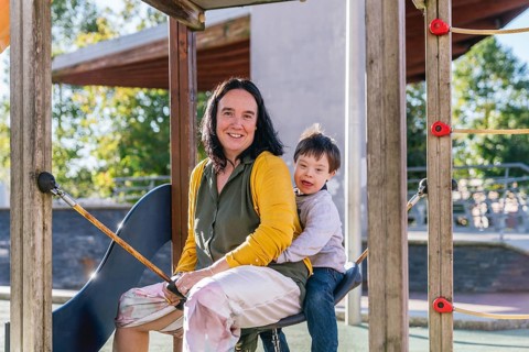 A joyful mother and child with Down syndrome are sitting together on a playground swing on a sunny