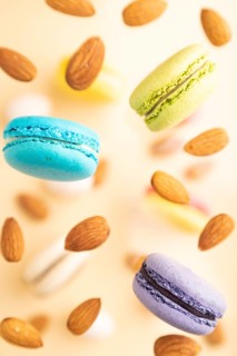 Multicolored flying macaroons and almonds frozen in the air on blurred beige background. top view,