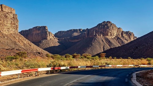 A road with a bend winds its way through impressive mountain scenery in a barren desert landscape