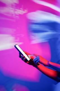 A hand interacts with a smartphone illuminated by vibrant neon lights, creating a modern and