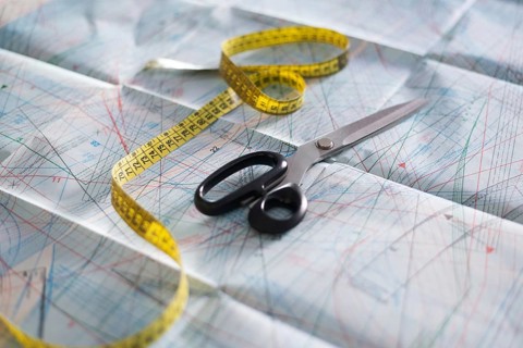 Scissors and a yellow measuring tape rest on detailed sewing pattern paper. This setup captures the