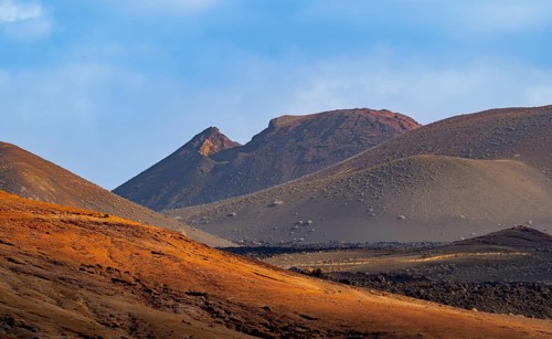 Scenic view of Timanfaya National Park's dramatic volcanic landscape with sunlit hills and rugged