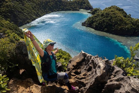 A traveler embraces nature on a cliff overlooking the stunning blue waters and lush greenery of
