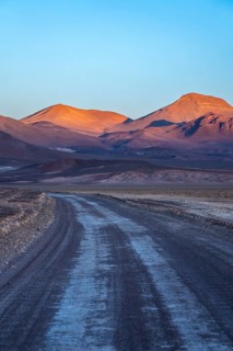 A serene evening view of a winding road meandering through the vibrant hues of orange-lit mountains