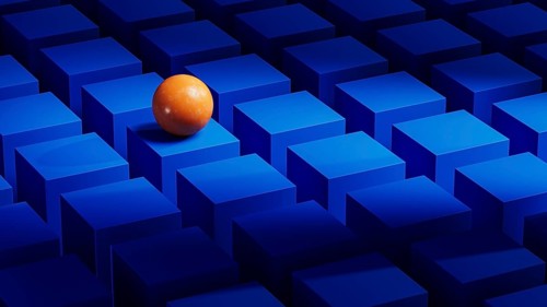 An orange sphere balances on a series of blue geometric forms. The abstract arrangement creates a