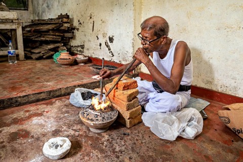 A man blows into a coal-fired pool with a concentrated face, a man burns sapphires in a small stove