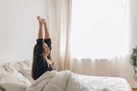 A woman stretches in bed, bathed in soft morning light, symbolizing a fresh start. The peaceful
