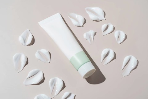 An elegant cosmetics container with a minimalist design appears next to artistic cream stains on a