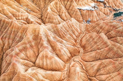 Aerial shot captures a striking desert landscape with rugged, eroded hills and vivid geological