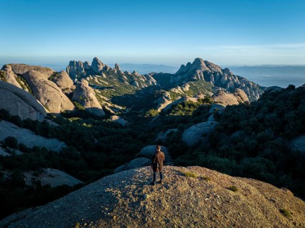 A person stands on a rocky hill, overlooking the stunning Montserrat mountains in Catalonia, Spain,