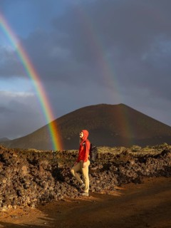 A woman in a red jacket stands on volcanic terrain in Timanfaya National Park, Lanzarote. A vivid