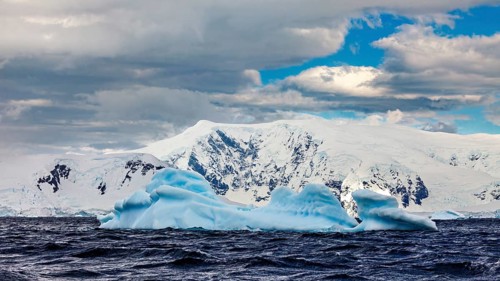 Icebergs floating in undulating water against a backdrop of snow-capped mountains under a dramatic