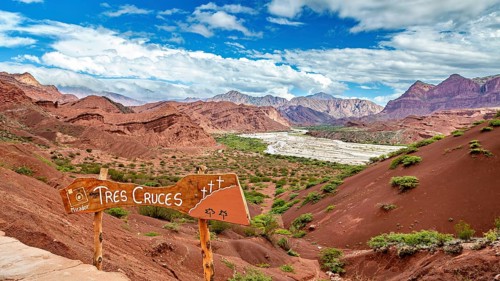 Red mountain landscape with vegetation and a sign in the foreground under a blue sky, The landscape
