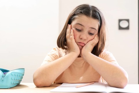 A young girl sits at a desk, appearing stressed and overwhelmed with her homework. Her head rests