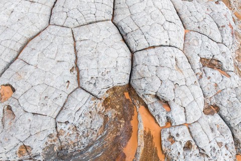Close-up view of abstract white rocks with deep, intricate cracks and contrasting orange hues. This