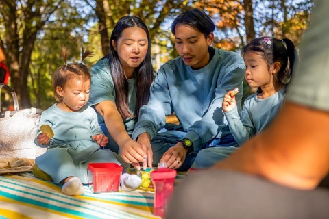 Asian family sharing a joyful picnic in a sunlit autumn park. They are seated on a blanket