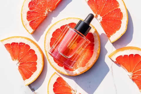 A glass dropper bottle with a black cap, placed on fresh grapefruit slices. The bright citrus and