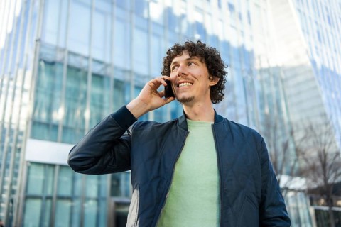A businessman holds a phone to his ear while walking outside a modern glass building. The image