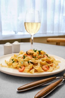 A plate of seafood pasta with shrimp and clams on a kitchen table. A glass of white wine stands