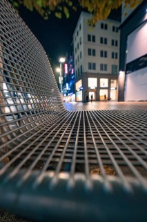 Night shot of a modern bank in a city street with illuminated shops in the background, Stuttgart,