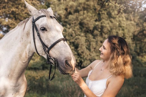 A young woman gently interacts with a white horse in a tranquil outdoor countryside environment.
