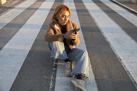 A Mixed-race woman sits quietly at a crosswalk, absorbed in her smartphone Natural light enhances