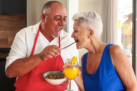 A joyful senior couple engages in a playful and affectionate interaction in a bright kitchen during