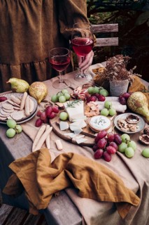 A rustic setup featuring a delicious cheese and fruit platter paired with two glasses of red wine.