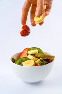 Introducing ingredients from above with a woman's hand, recipe for a fruit salad with kiwis,