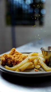 A close-up shot of crispy golden fries and crunchy chicken pieces on a plate. Fresh herbs are