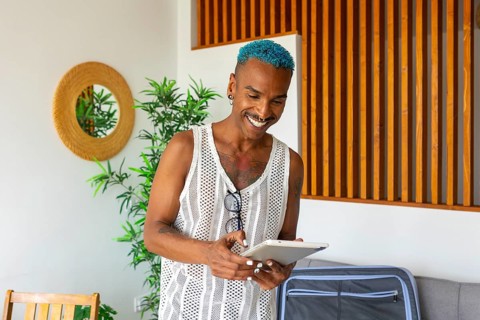 Hispanic LGBTQIA+ man with blue hair happily prepares for holidays using a tablet, surrounded by