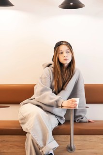 Teenage girl in casual attire with a cap, sitting thoughtfully on a bench. She holds a paper cup,