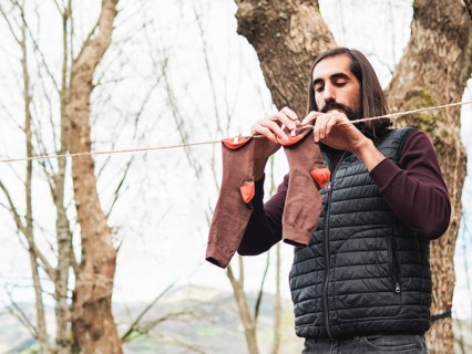 A man hangs clothes on a line in a forest, emphasizing simplicity and nature. The scene highlights