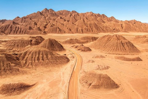 Aerial view of a vast desert landscape featuring a rugged mountain range and a winding dusty road