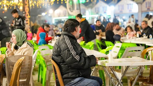 Muslim families and individuals gather at outdoor tables for a mass community Iftar meal under